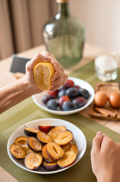 Person squeezing lemon juice on sliced plums, preparing ingredients for plume pie bakery. Authentic lifestyle home cooking process