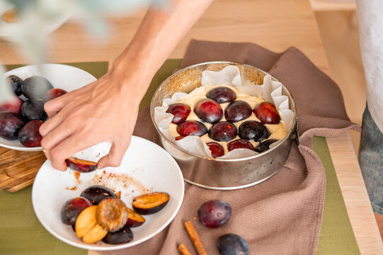 Sweet fruit seasonal plum cake cooking process, person placing plum halves into baking pan with dough, soft selective focus, authentic lifestyle