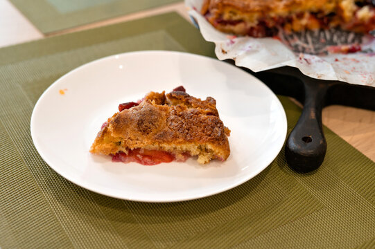 Piece of baked famous plum torte with golden brown crust on plate, authentic lifestyle home recipe, soft selective focus. Traditional fruit seasonal food