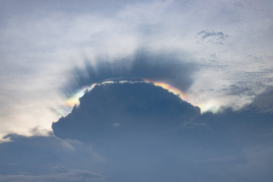 Dark storm cloud with glowing rainbow edge beneath textured overcast sky, creating dramatic atmospheric weather scene with soft natural light and tranquil mood