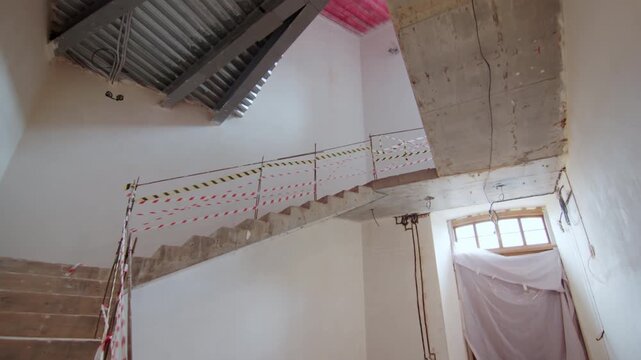 Dilapidated staircase with wooden handrail leads upwards. Hazard tapes hang from handrails of staircase warning of dangerous steps