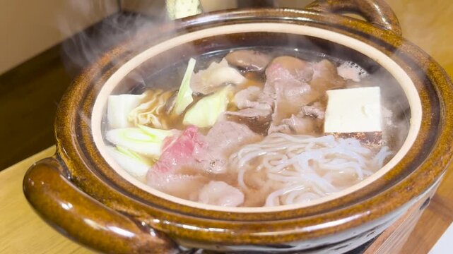 温泉宿の贅沢な食事 湯気が立ち上るアツアツの土鍋料理（肉鍋）のシズル感