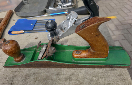 Vintage hand plane with green metal body and wooden handle on a table with other tools