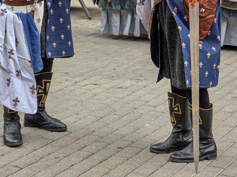 Footwear of a parade participant in medieval attire showing sturdy black leather boots with gold cross symbol