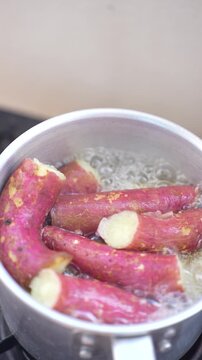 Red-skinned sweet potatoes boiling in a pot of bubbling water on a stove
