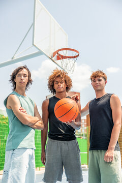 vertical Multicultural male friends posing with basketball on court