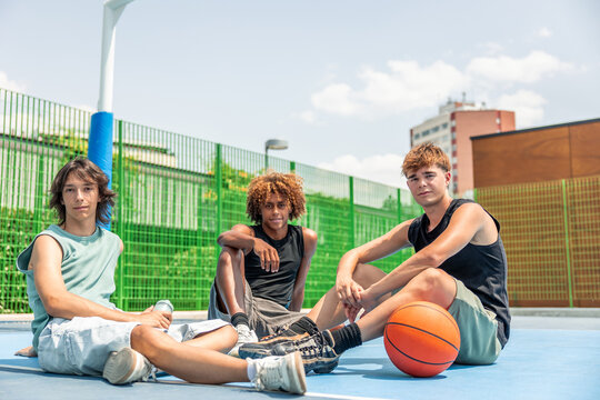Multicultural young friends resting on basketball court