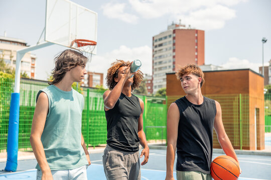Multicultural young men drinking water after basketball game
