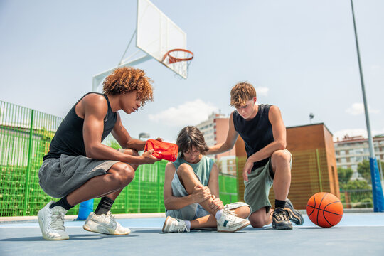 Multicultural friends supporting injured boy on basketball court