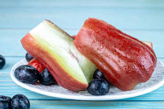 Fresh sliced red wax apple garnished with blueberries on a white plate with blue background.
