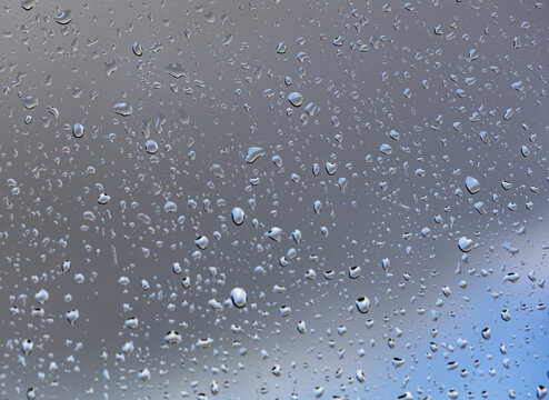 Raindrops cling to a glass pane, forming clusters and streaks