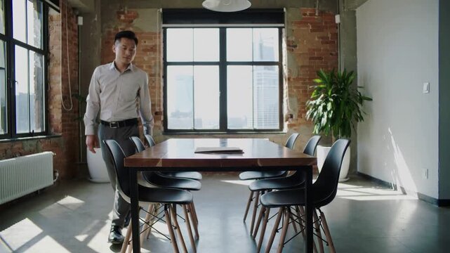Entering businessman in light shirt placing tan folder on table in loft meeting, to present