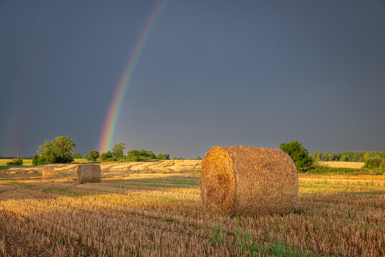 Serene sunset rainbow across a harvested rural field after rain.