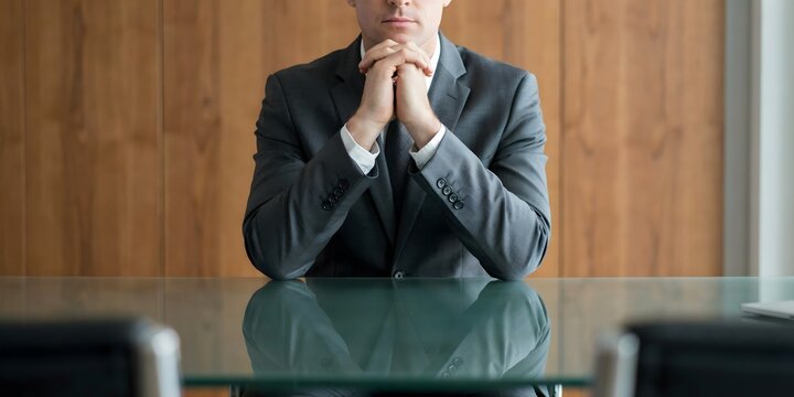 Thoughtful Businessman Sitting At Office Desk With Hands Clasped In Deep Reflection And Decision