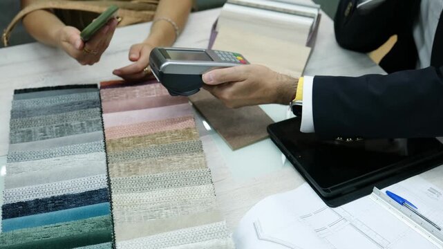 Customer paying with smartphone using NFC technology while choosing fabric samples with a designer