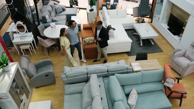 Salesman consulting a young couple buying a sofa in a large furniture showroom