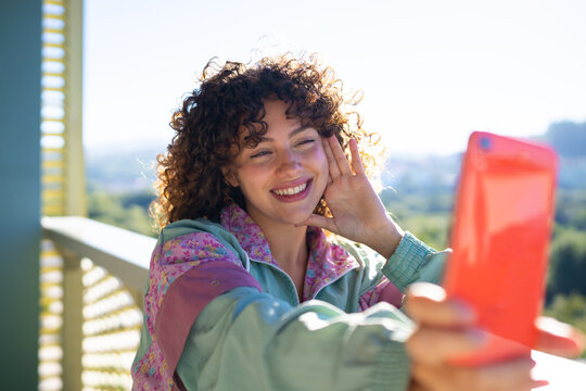 White woman with curly hair taking a selfie outdoors