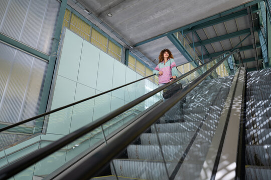 White woman traveling with suitcase on escalator in modern building