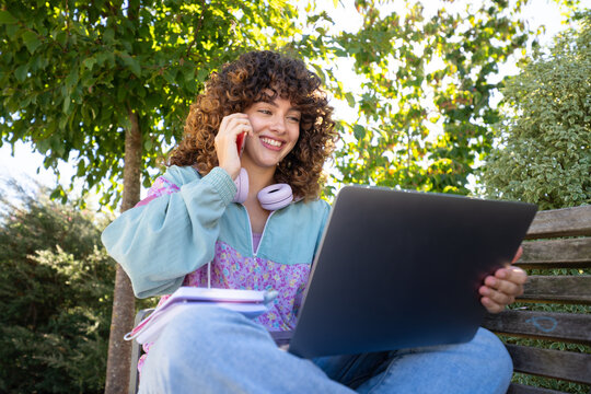 White woman using laptop and phone outdoors on park bench