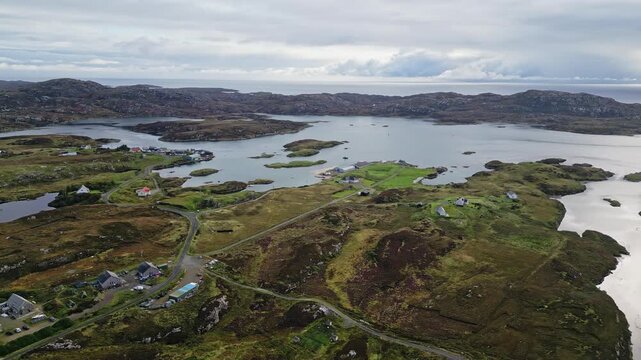 Cinematic aerial, Grimsay near North Uist in the Outer Hebrides, Scotland, showing remote homes, winding roads, coastal water, secluded properties and rugged island landscape