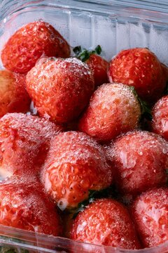 Fresh strawberries in clear container with ice crystals at a market