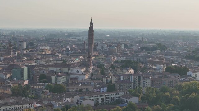 Cremona skyline reveals Torrazzo, Cathedral complex and dense historic neighborhoods during widening aerial movement across Po Valley, Lombardy, Italy, drone orbit pullback.