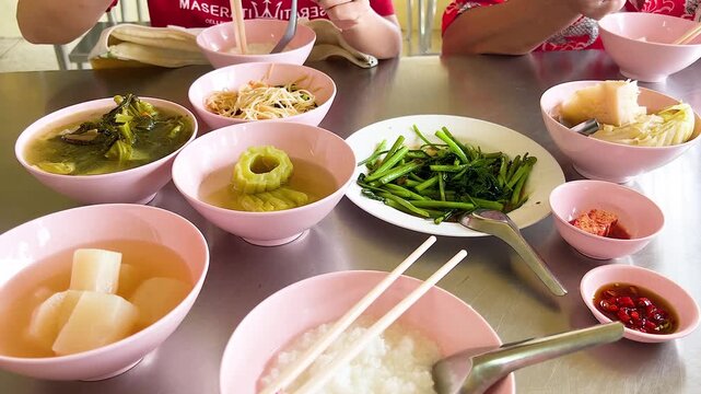 Asian family enjoying traditional rice porridge breakfast with various side dishes in local restaurant setting.