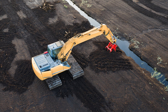 Aerial view of crawler excavator digging drainage ditch on peat bog extraction field during harvesting production process in Estonia
