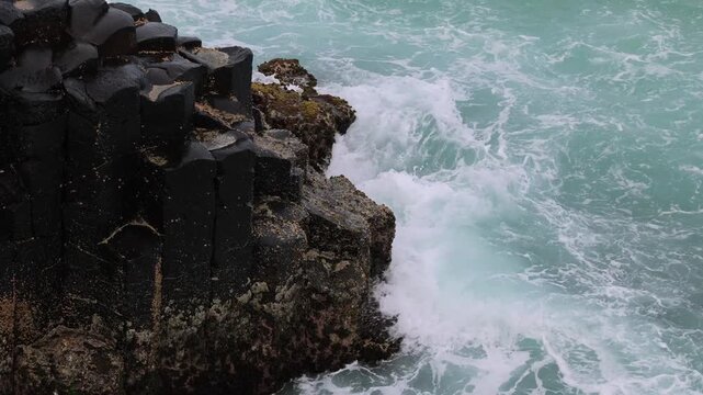Waves crashing against basalt columns at coastal cliff during ocean storm.