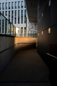 Dark architectural ramp with concrete walls, handrail and warm light at the far end, creating a minimalist walkway with strong perspective and depth
