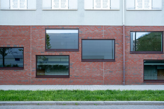 Red brick facade with rectangular windows, pale upper wall and green grass, forming a geometric architecture pattern across a quiet building exterior