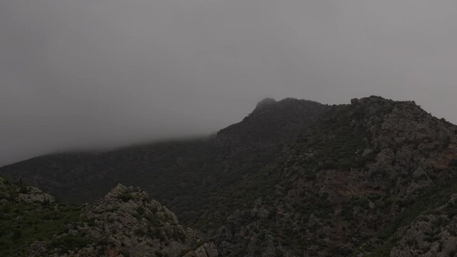 A close-up timelapse video of clouds passing over a mountain on a foggy day.