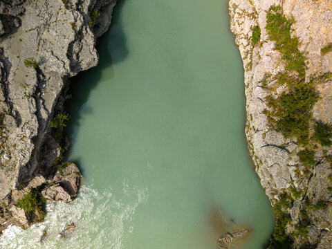 Vjosa River, Albania runs between cliffs in striking canyon landscape. Aerial perspective reveals pale green water, rough stone sides, and exposed rock faces with patches of grass and scrub.