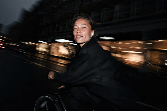 Smiling Woman Cycling Through City Street at Night with Motion Blur Lights