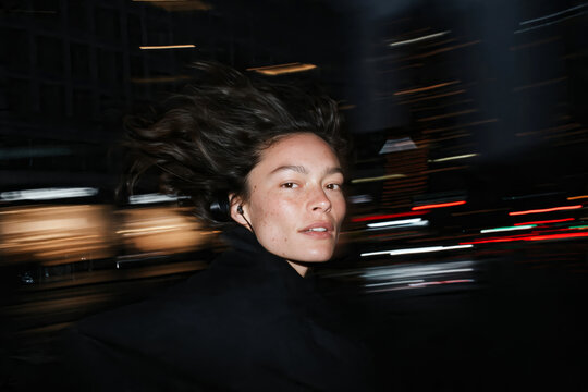 Smiling Woman Cycling Through City Street at Night with Motion Blur Lights
