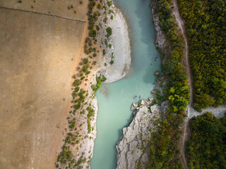 Fototapeta premium Vjosa River passes narrow canyon in Albania. Overhead perspective shows pale blue current, stony banks and green woodland, with serene wilderness character and vivid color contrast.