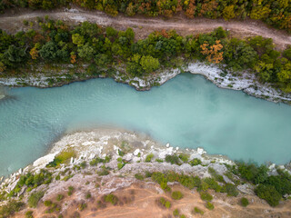Fototapeta premium Vjosa River in Albania flows beneath top down aerial perspective, bordered by chalky cliffs and green woodland. Calm turquoise channel gives this remote river landscape peaceful, scenic mood.