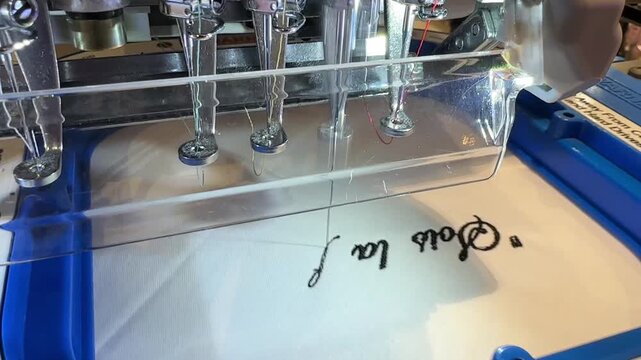 Automatic Industrial Embroidery Machine Stitching Custom Lettering on Fabric in Modern Textile Workshop Showing Precision Sewing Technology Manufacturing Production Personalization Automation 