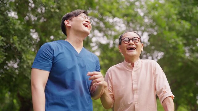Asian male caregiver walking with senior man in park, laughing and enjoying time together, elderly companionship, emotional support, active aging, mental wellbeing and home care