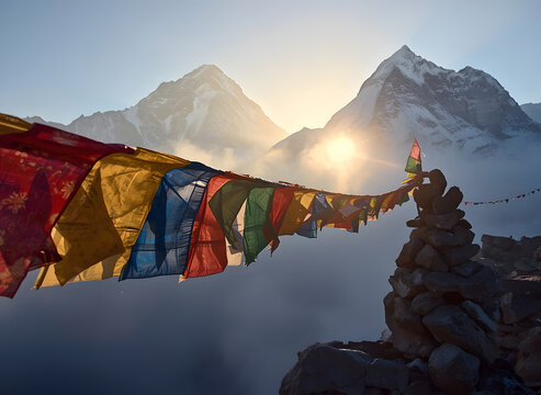 Colorful Tibetan prayer flags fluttering against misty Himalayan snow peaks at golden sunrise