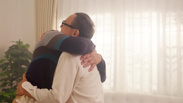 Happy Asian senior gay couple dancing and hugging together at home. Elderly family enjoying romantic moment, v mental wellbeing, love, active aging and joyful retirement lifestyle.