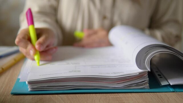 Close Up of Hand Highlighting Text in Open Document Folder with Yellow Marker Pen, Audit and Study Concept