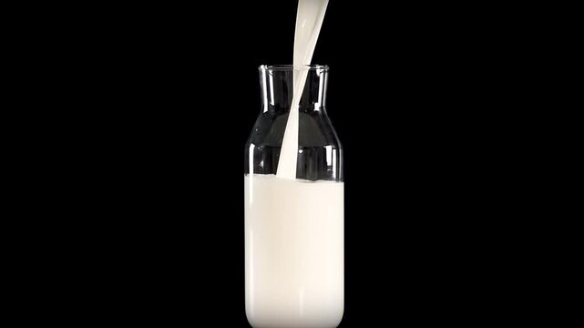 Fresh milk pouring into glass bottle close up slow motion footage isolated on black background.
