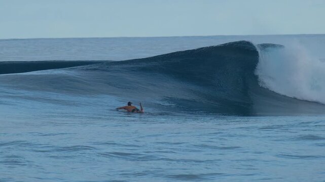 Surfer paddles towards the line up on the uncrowded surfing spot of the Sultans in the Maldives with the big and perfect glassy waves
