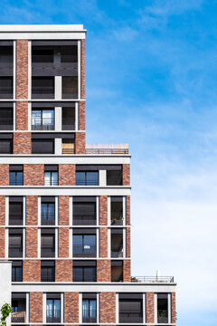 Modern residential architecture in La Confluence, Lyon, France, with a red brick apartment building facade rising against a vivid blue sky