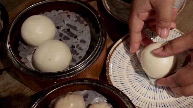 Close-up footage of hands opening a delicious steamed bao bun filled with sweet custard.