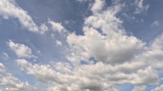 Beautiful time-lapse footage of white fluffy cumulus clouds moving across a bright blue sky on a sunny day.