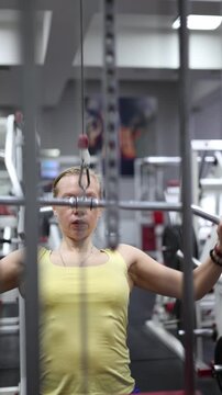 Vertical 4k video - middle-aged woman engage in pulldown training on a lat machine, showcasing her commitment to fitness and the importance of strength training in the gym.