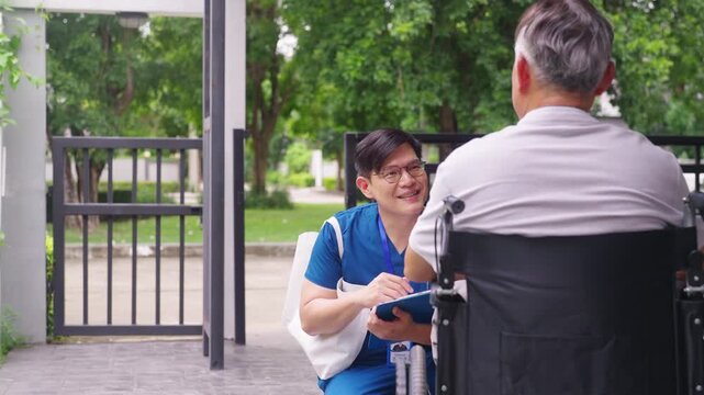 Asian male professional caregiver or nurse visiting senior man in wheelchair at home, asking about symptoms and checking health condition. Elderly home care, medical support and patient wellbeing