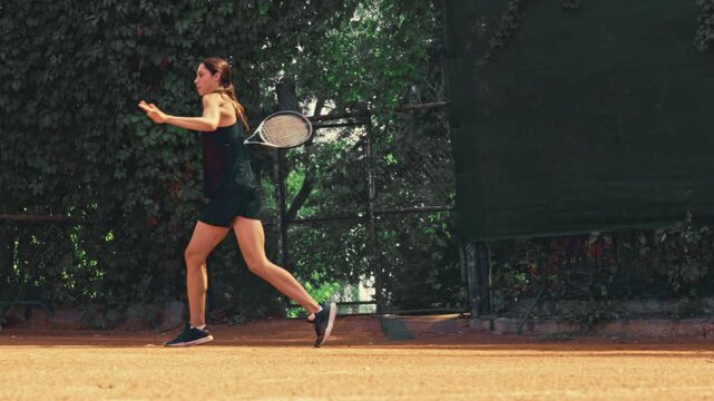 Skilled tennis woman starts with strong serve and plays active rally on outdoor clay court with confident focus. Women tennis, match preparation, fitness training concept.